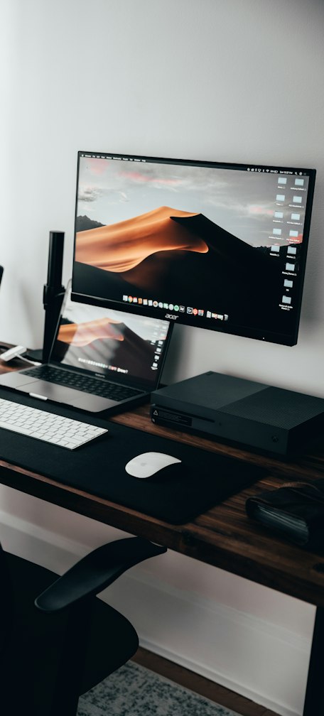 A home office workspace with a laptop, monitor, and keyboard on a wooden desk