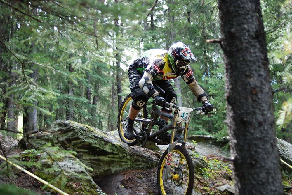 A downhill rider in a full-face helmet on a forest trail: the sport and the scene the SICK! fan base lives for.